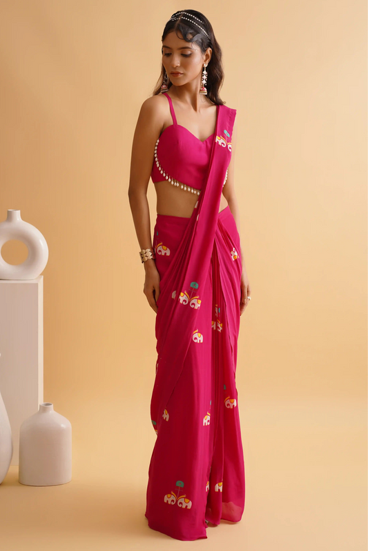 A woman posing in a fuchsia pink saree with a traditional hathi-palki print and a solid heart blouse with lace details.