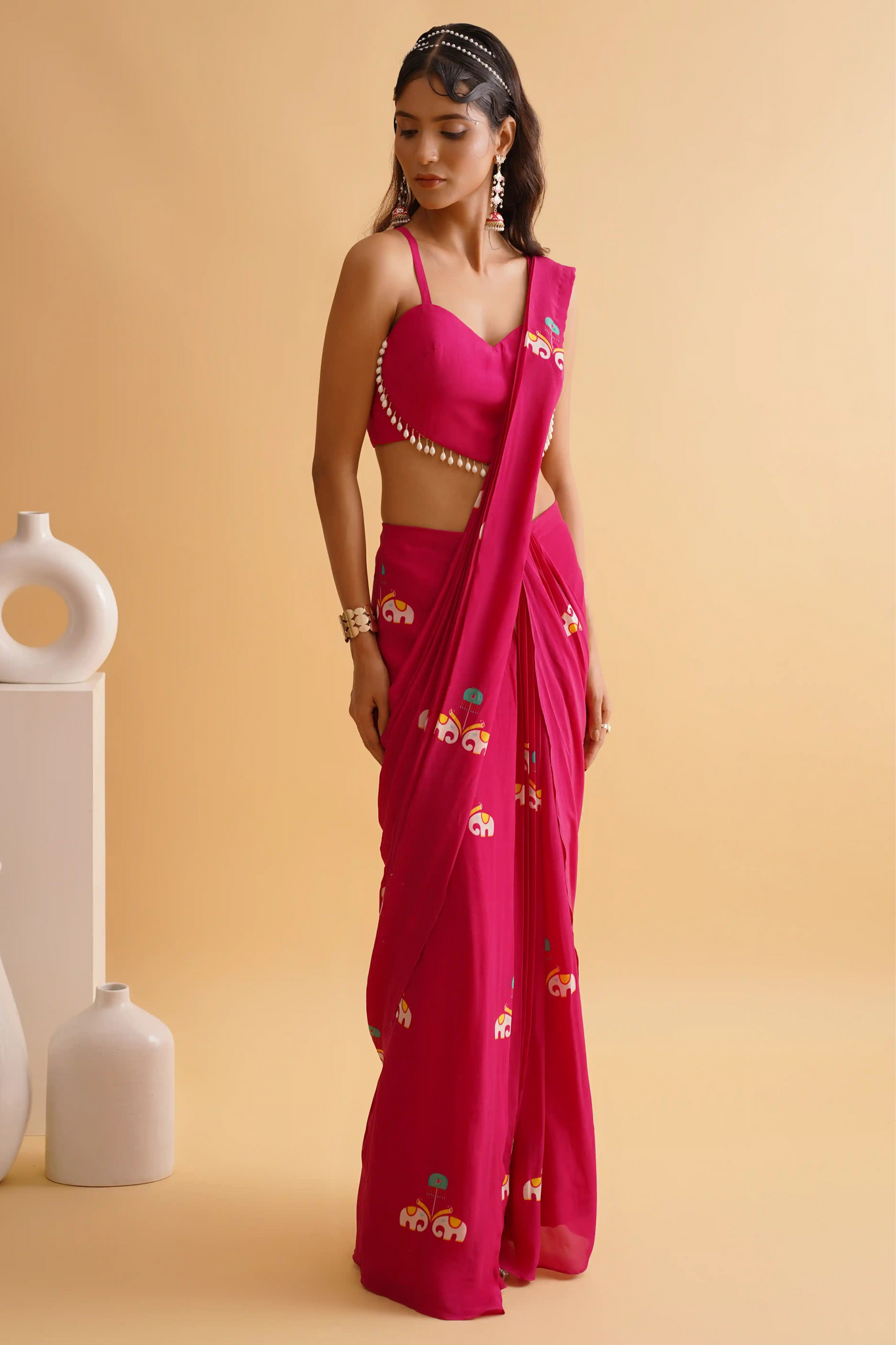 A woman posing in a fuchsia pink saree with a traditional hathi-palki print and a solid heart blouse with lace details.