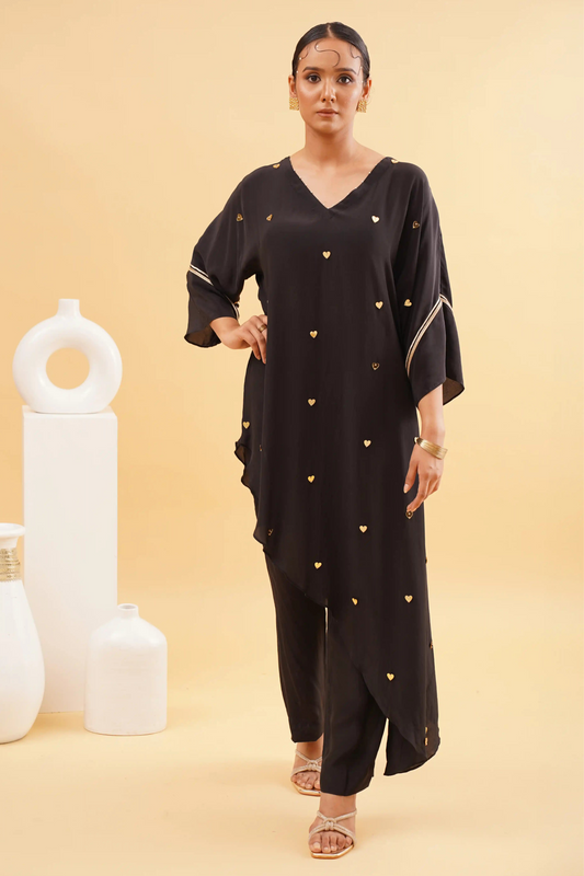 A woman wearing a chic black kaftan with mini heart embroidery and matching pants, standing against a neutral background.