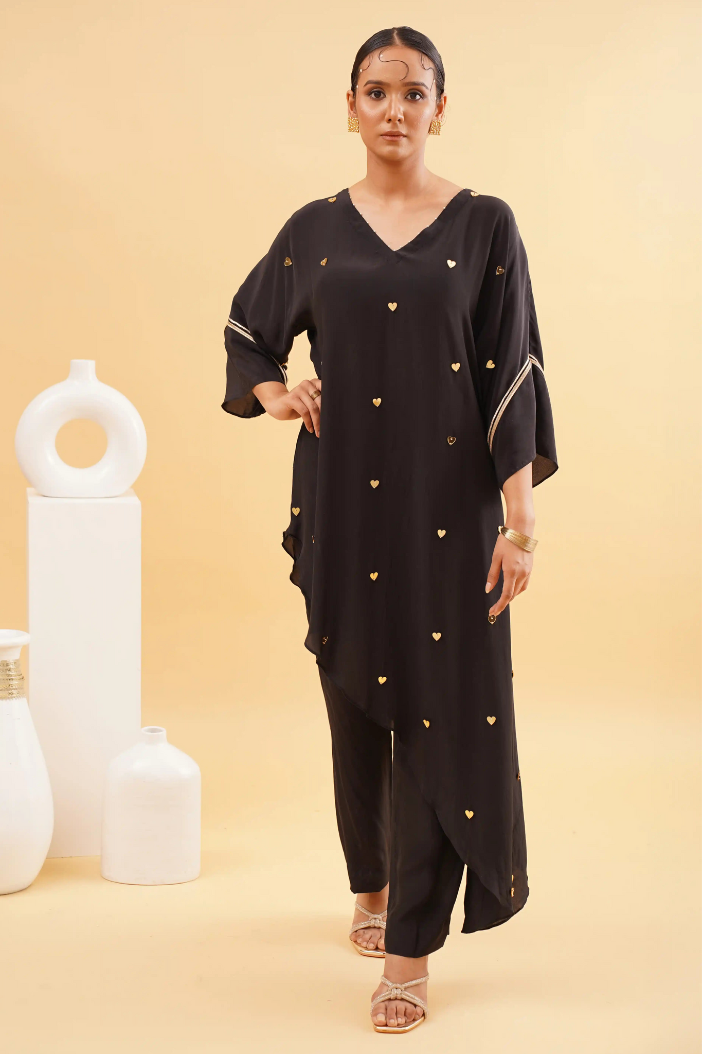 A woman wearing a chic black kaftan with mini heart embroidery and matching pants, standing against a neutral background.